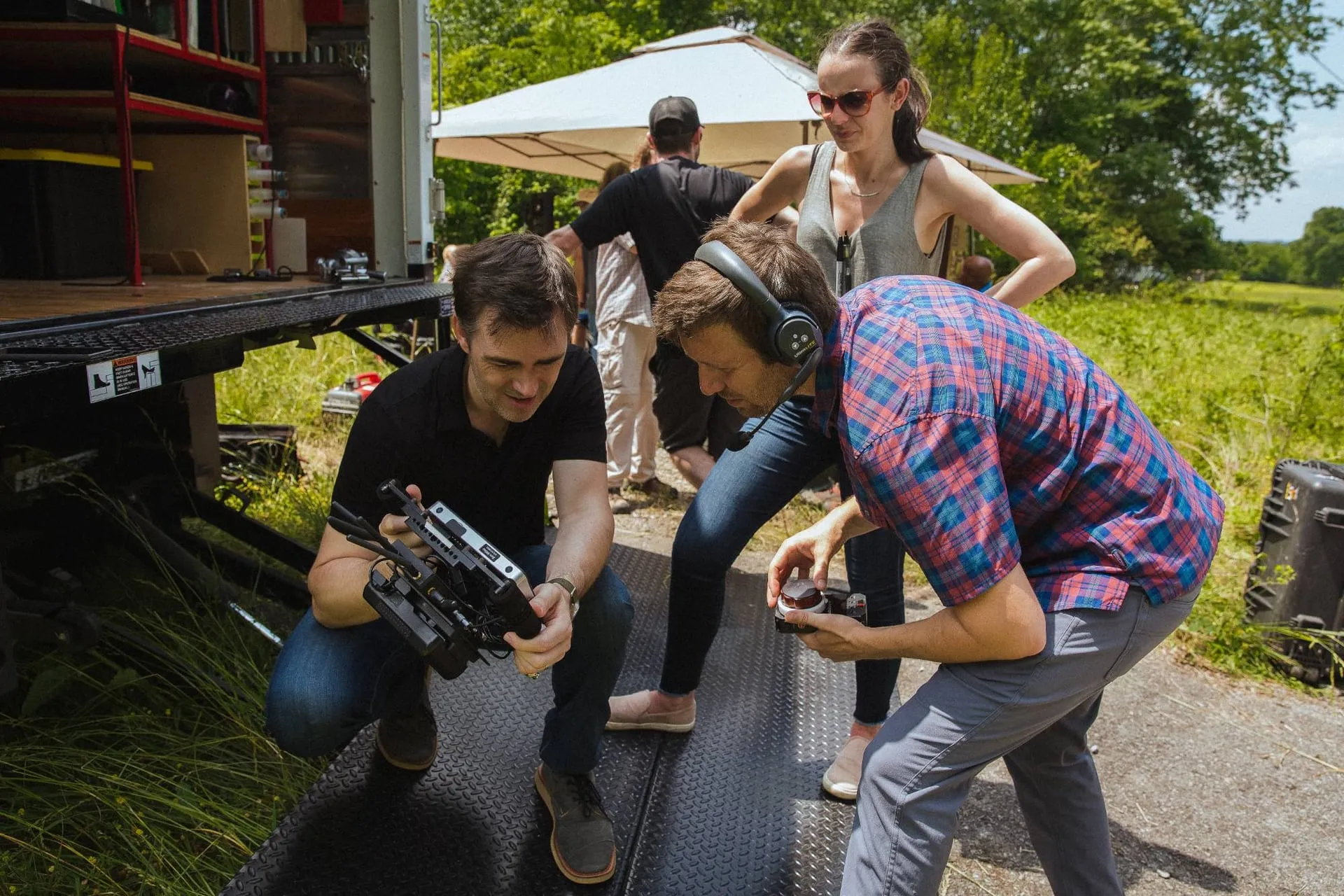 Two crew members crouched over a small monitor beside the grip truck, one in a headset, a third looking on.