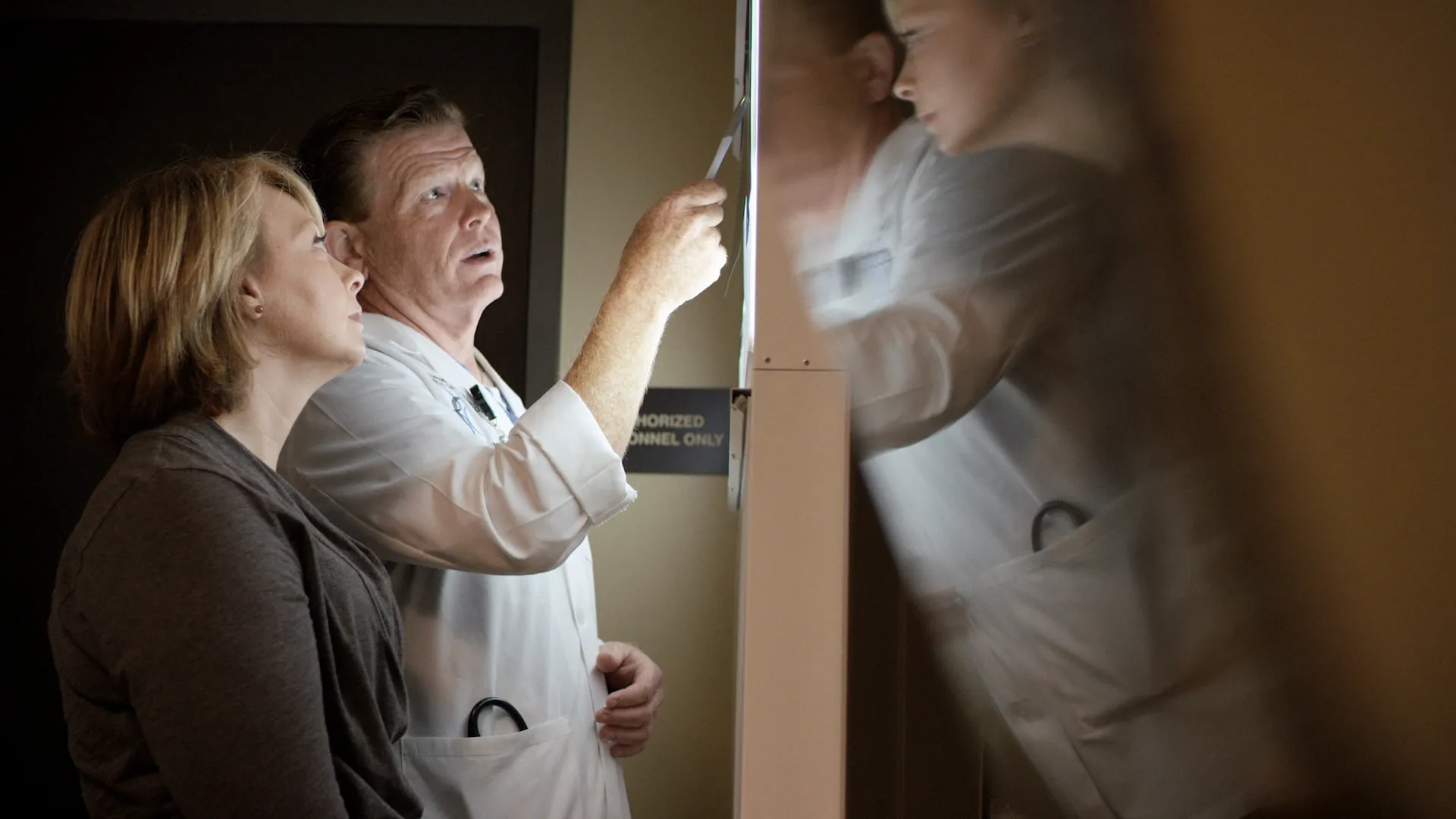 A doctor points out a scan on a light box as a patient looks on beside him.
