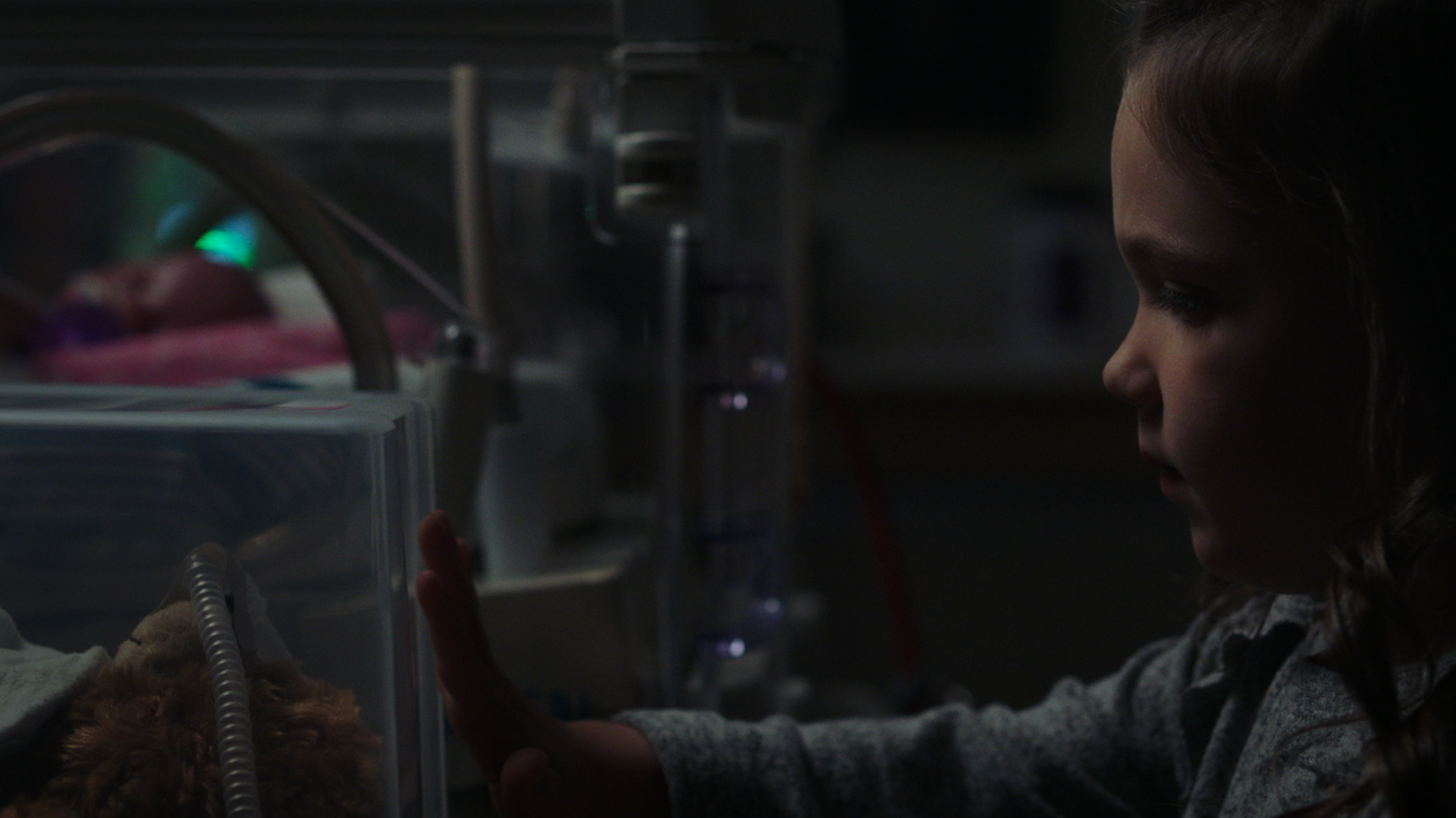 little girl looks into incubator where her preemie brother lies