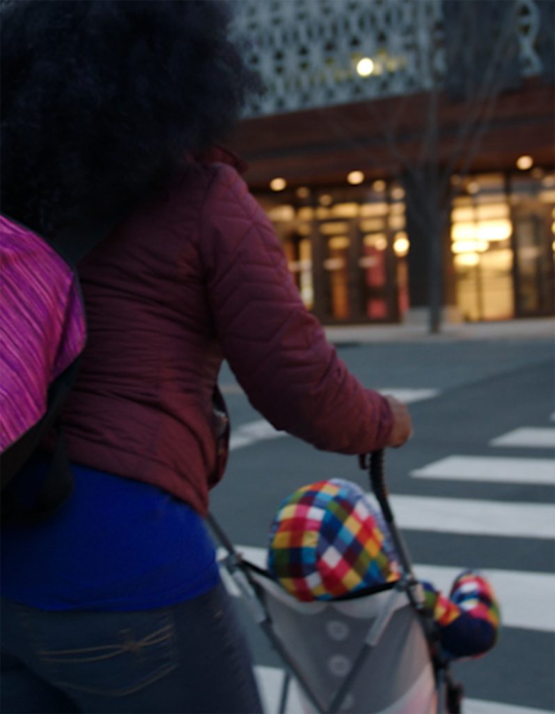 woman walks across street with baby in stroller