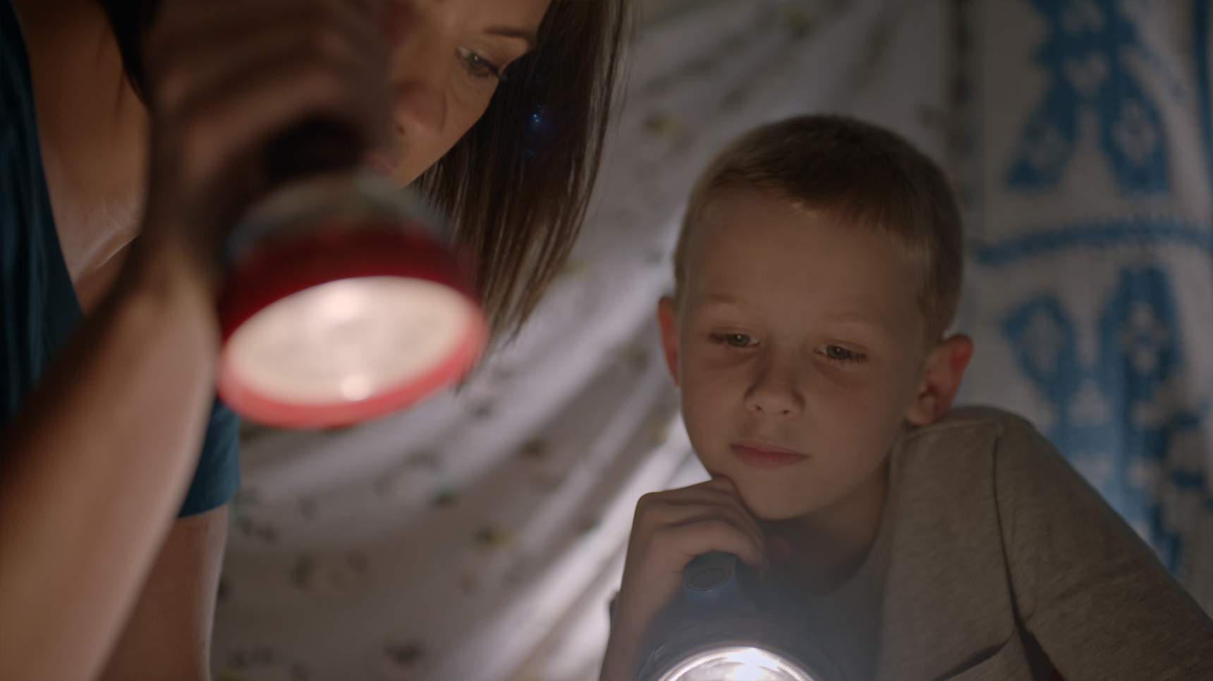 mother and son read book in tent with flashlights in his bedroom